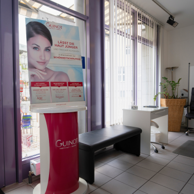 Heller Eingangsbereich des Kosmetikstudios mit Werbestand von Guino.